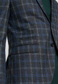 Kariertes Blazerjacke in Dunkelgrau und Blau, mit einem Ein-Knopf-Verschluss, mit Reverskragen und einer Leistentasche auf der linken Seite.