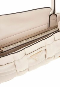 Sac à main en cuir beige matelassé avec une poche zippée dorée et un accent logo. L'intérieur présente une doublure lisse et une bordure contrastante.