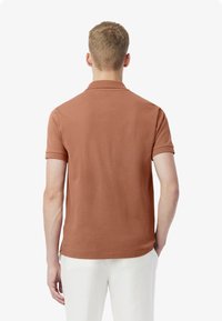 Rostfärgad polo med korta ärmar, en klassisk krage och en slät textur, i kombination med vita byxor.