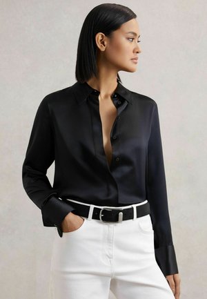 Czarna satynowa koszula z guzikami, z kołnierzykiem i długimi rękawami, zestawiona z białymi dżinsami i czarnym paskiem z srebrną klamrą.