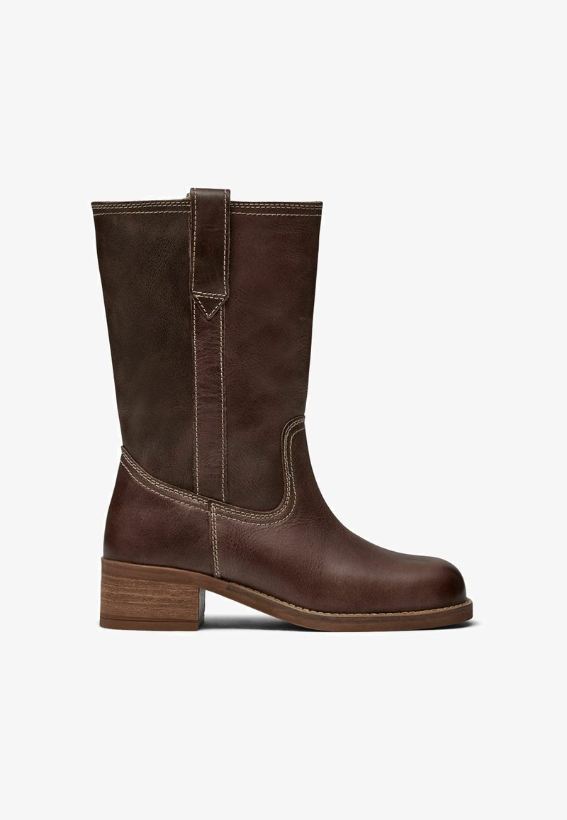 Botte en cuir brun mi-mollet avec languette de tirage, surpiqûres contrastées, bout arrondi et petit talon bloc en bois.