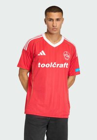 Camiseta de fútbol roja hecha de tejido ligero. Presenta un cuello en V blanco, un diseño a rayas y el logo "toolcraft" en blanco en la parte delantera.