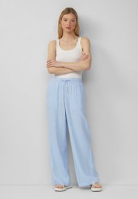 Helle, weite Hosen aus weichem Stoff mit elastischem Bund und Kordelzug. Kombiniert mit einem weißen Trägershirt und flachen Sandalen.