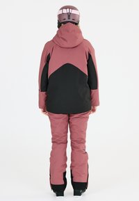 Rosa och svart skidjacka med huva, med ett geometriskt mönster. Matchande rosa skidbyxor med svarta accenter och dragkedjor vid ärmsluten.