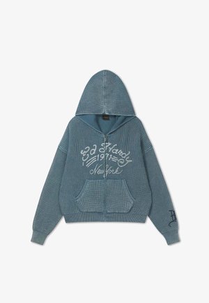 Blå strikket hættetrøje med lynlås, forlommer og hvid skrift med teksten "Ed Hardy 1971 New York" på brystet og ærmet.