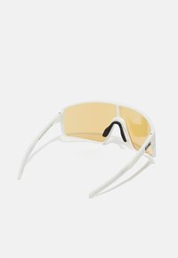 Lunettes de sport blanches avec un design surdimensionné, verres teintés jaunes, coussinets de nez noirs et branches fines blanches. Logo imprimé sur le côté.