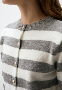Grau und weiß gestreifter Cardigan mit rundem Ausschnitt und strukturiertem Wollmaterial; mit dekorativen Knöpfen an der Vorderblende.