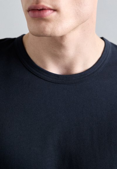 Mørk marineblå t-skjorte med rund hals, laget av ribbestrikket stoff med tettsittende passform, og med subtile sømdetaljer langs kragen og kanten.