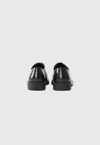 Zapatos de cuero negro con un acabado suave, puntera redondeada, suela de goma negra de bajo perfil y diseño minimalista.