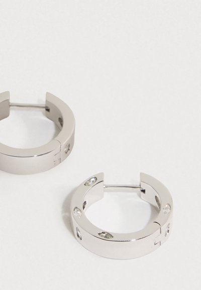 Paari läikivaid hõbedasi ringkõrvarõngaid, mille küljes on väikesed läbipaistvad teemandid, tavalise valge tausta peal.