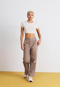 Világos bézs színű crop top laza, bézs színű cargo nadrággal párosítva. Az öltözet egyszerű dizájnnal rendelkezik, laza szabással és enyhén texturált anyaggal.
