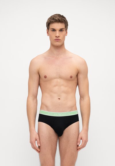Slip neri con una cintura verde con il testo "EMPORIO ARMANI". Il materiale sembra liscio e morbido, progettato per il comfort.