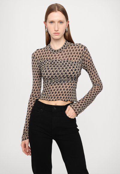 Durchsichtige Langarmbluse mit geometrischem Muster in Beigetönen und Brauntönen, mit einem kurzen Saum und einem runden Halsausschnitt. Kombiniert mit schwarzen Hosen.