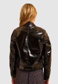 Chaqueta de cuero sintético negra y brillante con un silueta ajustada, cuello alzado y costuras visibles, llevada sobre un vestido de estampado floral.