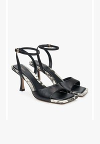 Zwarte leren haksandalen met dunne enkelbandjes, vierkante neuzen en een contrasterend slangenprintpatroon op de zolen.