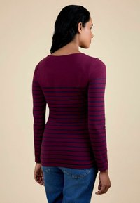 Cămașă cu mânecă lungă, de culoare vinie, cu dungi bleumarin, având un decolteu rotund și o siluetă ajustată. Design casual purtat cu blugi albaștri.