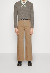 Pantalon large en velours côtelé marron, associé à un pull gris texturé et une écharpe vert menthe. Des chaussures noires complètent la tenue.