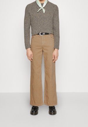 Bruine corduroy broek met wijd uitlopende pijpen, gecombineerd met een textuurgrijze trui en een mintgroene sjaal. Zwarte schoenen maken de outfit compleet.