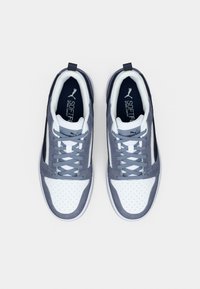 Ζεύγος λευκών και γκρι αθλητικών παπουτσιών Puma με κορδόνια, σε θέα από πάνω πάνω σε απλό ανοιχτόχρωμο φόντο.