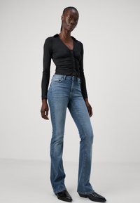 Maglia nera a maniche lunghe con dettaglio dei bottoni, abbinata a jeans a zampa d'elefante blu chiaro. L'outfit presenta un design elegante e sagomato con tessuto testurizzato.