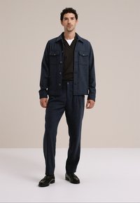 Pánská tmavě námořnická bunda se dvěma náprsními kapsami, doplněná o kalhoty ve stejném odstínu. Vícevrstvý materiál, jednoduchý design, černé boty, neutrální spodní tričko.