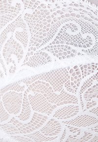 Tissu en dentelle blanche présentant des motifs floraux intriqués avec une finition texturée. Le design comprend des sections en maille ouverte pour un aspect délicat.