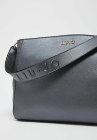 Borsa a tracolla in pelle grigio scuro con logo in rilievo sulla tracolla, forma strutturata, texture liscia e dettagli in hardware color oro.