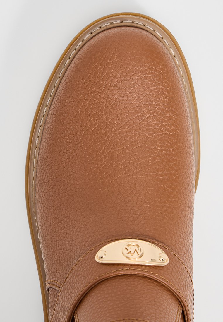 Bruine leren schoen met een gestructureerd oppervlak, ronde neus, gestikte zool en een klein gouden metalen logo op de voorkant van de band.