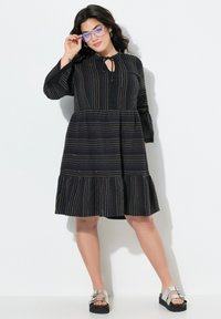 Robe noire avec des rayures colorées, décolleté rond et manches trois-quarts. Dotée d'un bas à volants et d'un détail en forme de clé au niveau du cou.