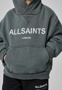 Felpa con cappuccio grigio scuro con tasca a marsupio, scritta bianca "ALLSAINTS LONDON" e polsini a coste. Tessuto morbido e strutturato, caratterizzato da un design classico.