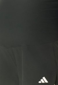 Pantalones cortos deportivos negros de material ligero, con una textura suave y un logo de Adidas en blanco. El diseño es minimalista y funcional.