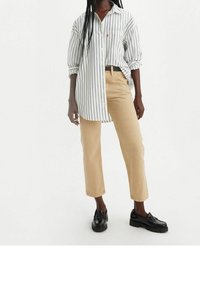 Camisa de rayas blancas y negras con botones en la parte delantera, combinada con pantalones rectos de un beige claro y mocasines negros.