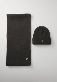 Conjunto de bufanda y gorro de punto negro, con una textura acanalada y un logo amarillo en ambas piezas. El gorro tiene un diseño de puño doblado.