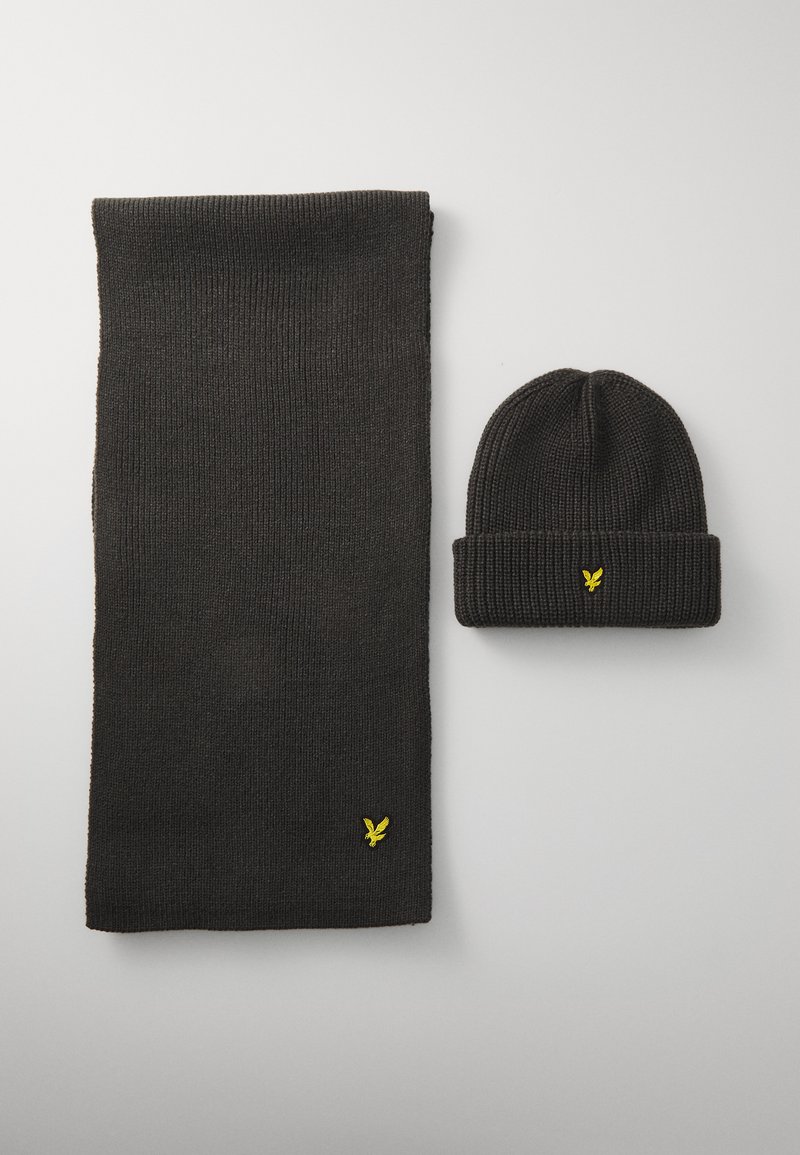 Conjunto de bufanda y gorro de punto negro, con una textura acanalada y un logo amarillo en ambas piezas. El gorro tiene un diseño de puño doblado.
