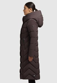 Lunga giacca a dolore marrone con motivo a zigzag, tasca laterale con zip e grande cappuccio. Realizzata in un tessuto liscio e imbottito con una toppa del logo rinforzata.