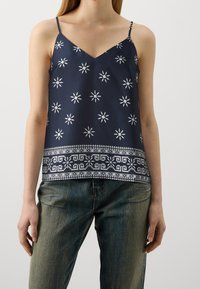 Marineblå cami-top med vitt stjärnmönster, V-ringning och spaghettiband; har en mönstrad kant vid nederkanten.