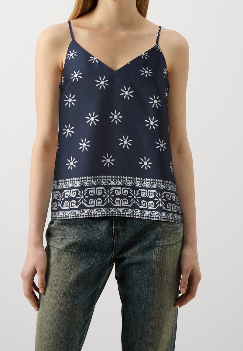 Marineblå cami-top med vitt stjärnmönster, V-ringning och spaghettiband; har en mönstrad kant vid nederkanten.