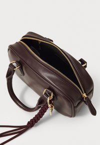 Dunkelbraune Lederhandtasche mit goldfarbendem Reißverschluss, der teilweise geöffnet ist, zwei Griffen und einer geflochtenen Quaste, die an einem Griff hängt, auf einem weißen Hintergrund.