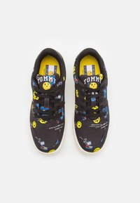 Zapatillas negras con caras sonrientes coloridas, lazos azules y patrones de bandera rojo-blanco-azul, suelas blancas y la marca "Tommy" en las lengüetas.