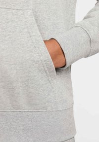 Harmaa vetoketjullinen huppari, jossa on kengurutasku. Sisältää teksturoitua kangasta, ribbauskuitua hihoissa ja yhtenäisen värin lähikuvassa.