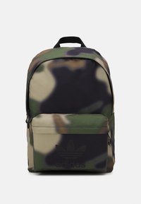 Adidas ryggsäck med kamouflage-mönster, framficka med dragkedja och svart handtag mot en vit bakgrund.