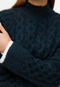 Dark blue knitted sweater with a cable pattern, featuring a high ribbed collar and thick ribbed cuffs, made from soft, textured fabric.