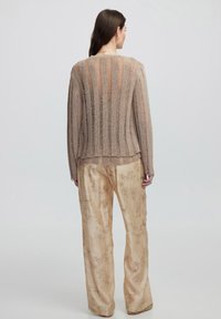 Beige pletený svetr s vertikálními pruhy a otevřeným pletením, v kombinaci s světlými, texturovanými kalhotami s širokými nohavicemi, které mají květinový vzor.