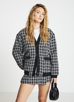 Schwarz-weißes Tweed-Jackett mit übergroßem Schnitt, zwei Fronttaschen und großen Knöpfen, kombiniert mit einem passenden Minirock und einer schwarzen Handtasche.