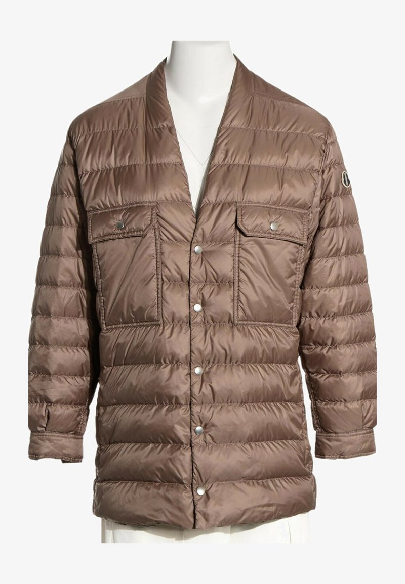 Veste matelassée marron avec fermeture par boutons-pression, deux poches avant à rabat et un écusson logo sur la manche gauche, présentée sur un mannequin blanc.