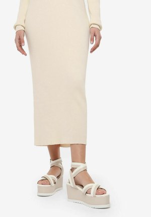 Sandalias de plataforma beige con múltiples tiras entrelazadas y un ancho tacón de cuña. La textura es suave con un acabado mate.