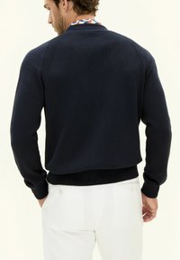 Marinblå stickad tröja med ribbade mudd och nederkant. Halsringningen har en färgglad design. Bärs över ljusa byxor.