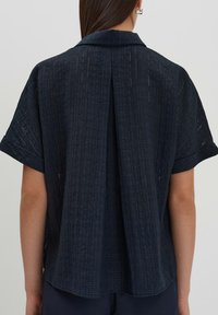 Maglietta corta blu scuro con maniche corte, caratterizzata da un motivo testurizzato, colletto e una vestibilità ampia con una cucitura centrale sul retro.
