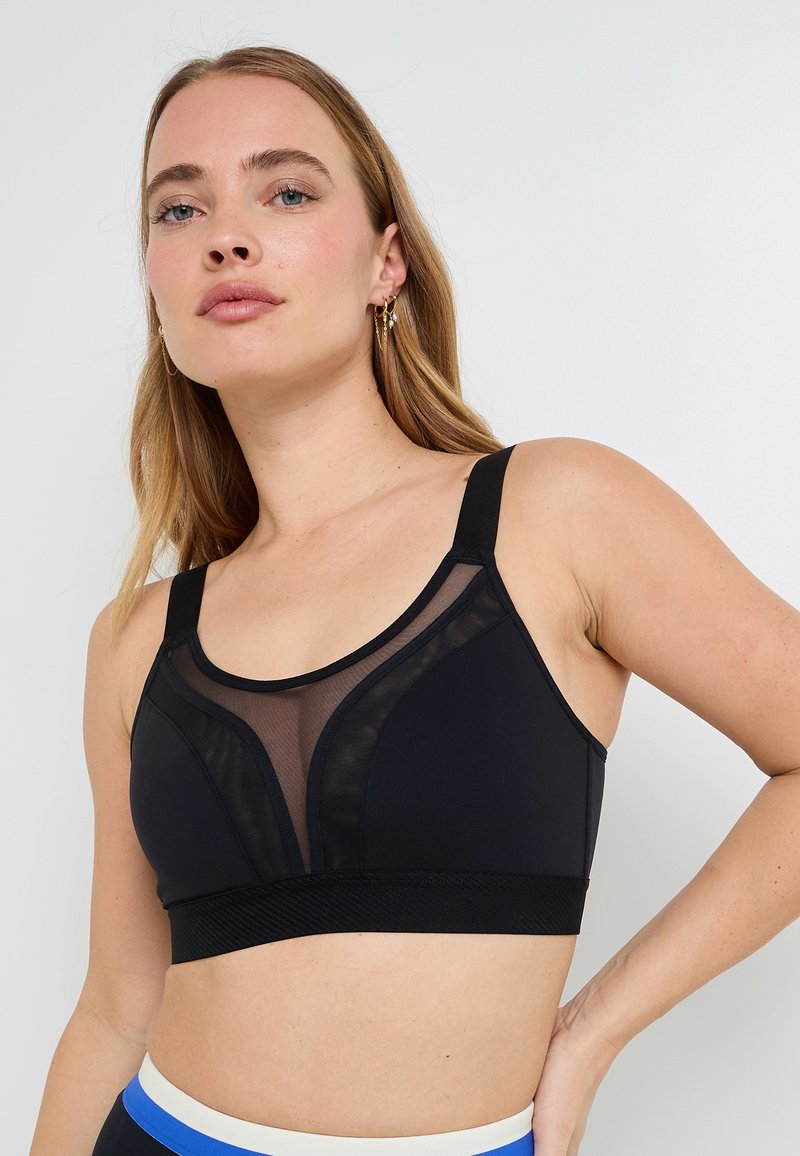 Reggiseno sportivo nero con design a pannello in rete, spalline larghe e fascia testurizzata. Tessuto liscio con vestibilità atletica e dettagli sottili.