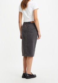 Svart denim midi kjol med passform, bakfickor och en brun läderetikett på midjan. Bärs med en vit t-shirt och svarta skor.